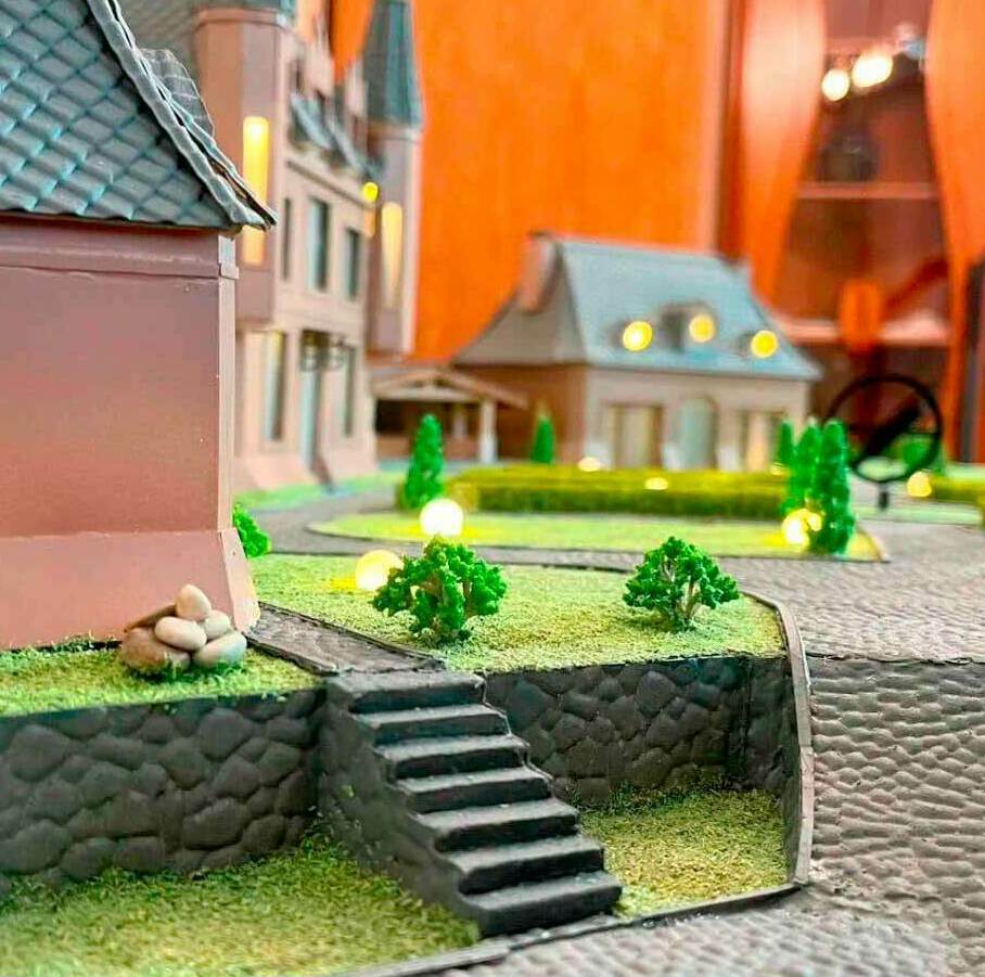 Изображена лестница на второй ярус прилегающей территории, тротуарные дорожки, зелёные газоны с кустами и сам дом