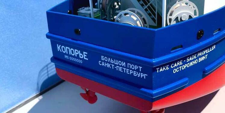 3‑D масштабная модель морского судна с детализированной надстройкой, палубным оборудованием и оранжевой спасательной шлюпкой: демонстрационная миниатюра для выставок, проектных презентаций и музейных экспозиций 3‑D масштабная модель фрагмента палубы морского судна: зелёная палуба, белые леерные ограждения и трапы, оранжевая спасательная шлюпка на штатных креплениях, палубные механизмы (лебёдка, вьюшка), надстройка с дверными проёмами и вентиляционными решётками, навигационное оборудование на верхней площадке; высокая детализация оснастки и конструктивных элементов