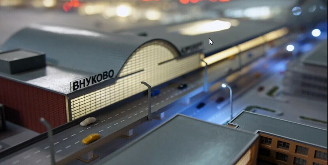 3D-масштабный макет терминала аэропорта «Внуково», демонстрирующий архитектуру главного здания с характерной арочной крышей и вывеской «ВНУКОВО». В композиции проработаны прилегающие дорожные развязки с миниатюрными моделями автомобилей, элементы уличного освещения, пешеходные зоны и прилегающие постройки. Макет передаёт масштаб и планировку территории аэропорта, включая подъездные пути, парковочные пространства и связь с городской инфраструктурой. Идеален для использования в презентациях инвестиционных проектов, архитектурных обзорах, планировании развития транспортной сети и образовательных целях.