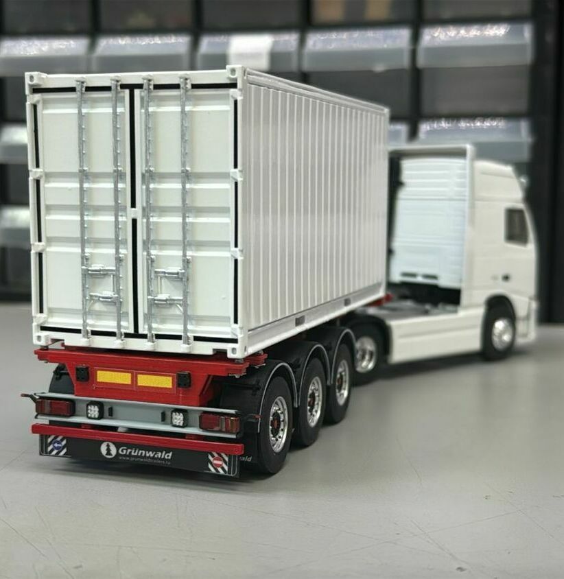 На фото изображён масштабный макет магистрального автопоезда:  • двухосный седельный тягач европейского типа; • трёхосный полуприцеп с рамой красного цвета; • установленный на полуприцепе съёмный кузов-фургон/контейнер с двустворчатыми задними дверями и запорными штангами.