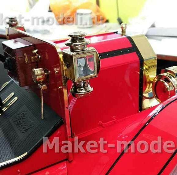 Масштабная модель старинного автомобиля Ford Model T 1914 года в ярком красном цвете с контрастными латунными деталями. Видны аутентичные элементы: массивная латунная фара с прозрачным стеклом, декоративные накладки, изящные рычаги управления, выразительные колёсные диски. Кузов украшен тонкими чёрными линиями, подчёркивающими контуры. Модель отличается высокой степенью детализации — от текстуры капота до мелких крепёжных элементов. Идеальный экспонат для музея или презентационного стенда, демонстрирующий инженерную мысль и эстетику автомобильного дизайна начала XX века. Изготовлена на заказ с сохранением всех исторических особенностей.