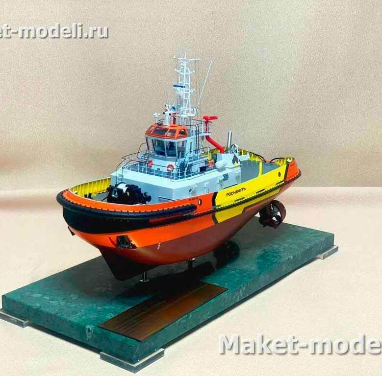 • Небольшой маневренный буксир на стационарной подставке с табличкой. • Корпус с мощным носовым кранцевым поясом по периметру, округлый нос — типично для швартовно-эскортных работ. • Надстройка с круговым остеклением, мачтой с РЛС и антеннами; на крыше — красный пожарный лафет. • На палубе: леерные ограждения, спасательные круги, буксирные кнехты/утки, швартовные устройства, буксирная лебёдка. • Главная особенность движителя: две выступающие из-под днища азимутальные колонки (Z-drive), обеспечивающие 360° вектор тяги. • Окраска в сигнальные оранжево-жёлтые тона; на борту видна надпись «Роснефть».  Назначение модели/прототипа: портовые швартовые и буксирные операции, эскортирование судов у нефтяных терминалов, аварийно-спасательные и противопожарные функции.