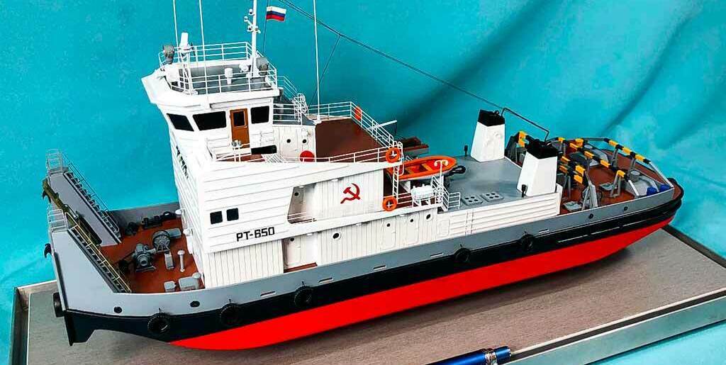 Масштабная модель речного буксира-толкача «PT-650» — детализированная сборная копия судна с символикой СССР, антеннами, палубным оборудованием и российским флагом, коллекционная модель для любителей судомоделизма, изготовленная на заказ в макетной мастерской Maket-modeli.ru Реалистичная модель буксира-толкача «PT-650» в масштабе: белый корпус с ярко-красной ватерлинией, детально проработанные надстройка, леерные ограждения, спасательные круги, палубные механизмы и дымовые трубы. На борту видна маркировка «PT-650», присутствует советская символика (серп и молот), а также российский флаг на мачте. Модель демонстрирует конструктивные особенности речных толкачей, идеально подойдёт для коллекционеров, музейных экспозиций, тематических выставок, посвящённых водному транспорту и истории судоходства.