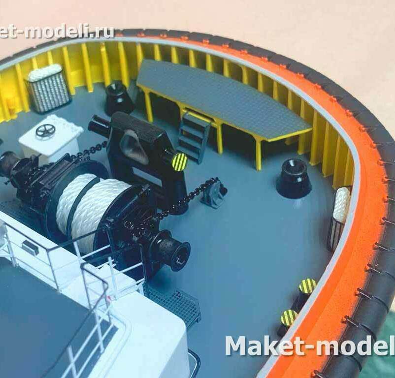 • Буксирная тросовая лебёдка с барабаном под синтетический канат и боковыми шпулями. • Буксирный клюз‑скоба (towing staple) для направления тягового троса. • Швартовые кнехты/тумбы и клюзы по бортам. • Киповые планки/направляющие для каната. • Палубный люк с запорным штурвалом. • Вентиляционные «грибки» (аэрационные оголовки). • Леерное ограждение и фальшборт. • Массовый резиновый кранцевый пояс (привальный брус) по периметру носа. • Переходная площадка/настил с трапом под фальшбортом.  Назначение узла: выполнение буксирных и швартовых операций с носа судна (эскорт/портовые работы), безопасное ведение и выборка буксирного троса.