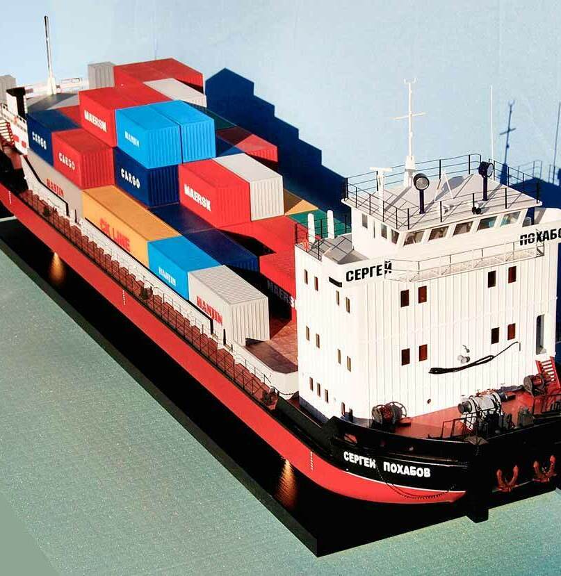 Масштабная модель грузового теплохода «Сергей Похабов» с контейнерами Maersk и Hapag-Lloyd — детализированная копия контейнеровоза для коллекционеров и музейных экспозиций, изготовленная на заказ в макетной мастерской Maket-modeli.ru Реалистичная масштабная модель грузового теплохода «Сергей Похабов», загруженного транспортными контейнерами ведущих мировых операторов — Maersk, Hapag-Lloyd, COSCO и других. Корпус судна выполнен в классической цветовой гамме: тёмно-красный с чёрной ватерлинией, надстройка — белая. На модели отчётливо видны детали: капитанский мостик с окнами, навигационное оборудование, лебёдки, швартовные устройства, спасательные круги. Контейнеры аккуратно уложены в несколько ярусов, создавая эффект загруженного международного рейса. Модель демонстрирует конструктивные особенности современных контейнеровозов и станет ценным экспонатом для морских музеев, учебных заведений или частной коллекции моделиста.