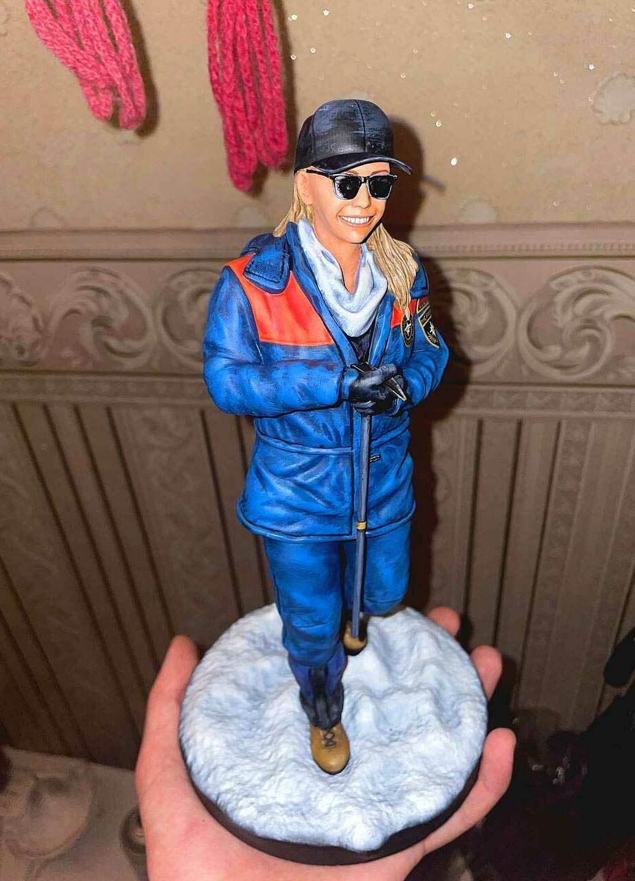 3D-фигурка человека-женщина в стиле уличного образа: кастомная статуэтка на заказ по фото, напечатанная на 3D-принтере — стильная поза с тростью, кепкой и солнцезащитными очками. Детализированная модель в сине-оранжевой куртке для коллекционеров и декора! Изготовленная для подарка Кастомная 3D-фигурка женщины, изготовленная по фотографии на 3D-принтере. Статуэтка изображает женщину в расслабленной, но выразительной позе с тростью в руке. Одета в стильную сине-оранжевую куртку, чёрную кепку, солнцезащитные очки, светлый шарф и практичные ботинки. Волосы распущены, на лице — уверенная улыбка. Фигурка установлена на круглой подставке с имитацией снежного покрытия. Пример персонализированной 3D-печати с высокой детализацией: проработаны черты лица, текстура одежды и аксессуаров. Подходит для украшения интерьера, коллекционирования или в качестве оригинального подарка.