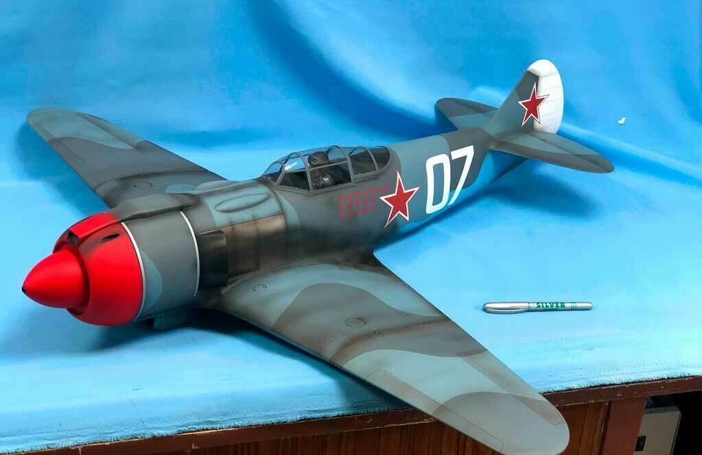 Детализированная масштабная модель советского истребителя Ла-5ФН, окрашенная в камуфляжные тона с ярко-красным носовым обтекателем. На фюзеляже и хвосте изображены красные звёзды, присутствует бортовой номер «07». Реалистичный макет с прозрачной кабиной пилота, идеально подходящий для коллекционеров, музейных экспозиций и тематических выставок.