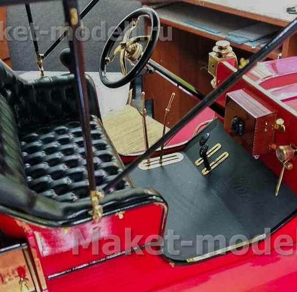 Масштабная модель старинного автомобиля с ярко-красным кузовом и контрастным чёрным кожаным салоном с тафтингом. Видны рулевое колесо с латунными вставками, приборная панель с классическими элементами управления, педали и декоративные латунные фонари. Модель отличается высокой детализацией — от обивки сидений до мелких крепёжных деталей. Идеальный экспонат для музея или презентационного стенда, подчёркивающий роскошь и стиль автомобильного дизайна прошлых эпох. Изготовлена на заказ с сохранением всех исторических особенностей.