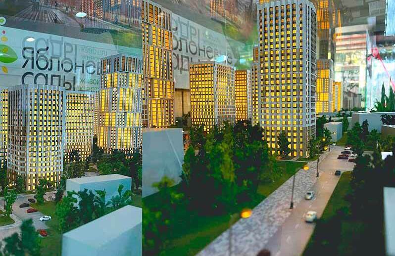 Детальный архитектурный макет современного жилого комплекса «Яблоневые сады», демонстрирующий плотную, но сбалансированную застройку. В центре композиции — несколько высотных жилых башен с подсвеченными окнами, создающими ощущение оживлённого городского пространства. Между зданиями проложены широкие пешеходные дорожки, окружённые миниатюрными деревьями и зелёными насаждениями. Видны элементы городской инфраструктуры: парковочные зоны, уличные фонари, дороги с макетами автомобилей. Проработаны детали дорожного покрытия, разметка парковочных мест, элементы благоустройства и ландшафтного дизайна. Макет передаёт концепцию комфортного жилья, где высотная застройка гармонично сочетается с зелёными зонами и удобной транспортной логистикой. Подходит для презентации градостроительного проекта, привлечения инвестиций и демонстрации планировки будущим жителям.
