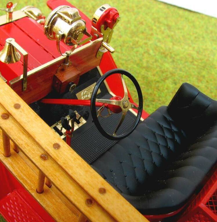 3D-масштабная модель коллекционного пожарного автомобиля Ford Model T 1914 года в масштабе 1:24. Видна передняя часть кабины с чёрным стёганым сиденьем, массивным рулевым колесом с красной рукояткой и латунными деталями управления. Присутствуют аутентичные элементы: фара в хромированном корпусе, колокол, рычаги и клапаны пожарного оборудования. Красные акценты сочетаются с полированными латунными вставками, подчёркивая винтажный стиль модели. Идеальный экземпляр для коллекционеров и любителей истории пожарной техники.