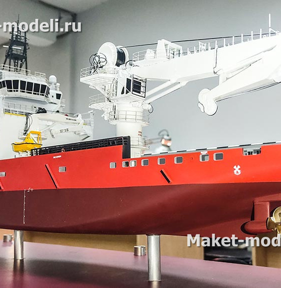3‑D масштабная модель судна обеспечения: красный корпус, белая надстройка, детализированные винторулевые колонки и палубное оборудование»Перед нами 3‑D масштабная модель судна обеспечения — высокодетализированная копия с красным корпусом, белой надстройкой, палубными кранами, спасательными шлюпками и винтами; экспонат размещён на опорах в выставочном пространстве.