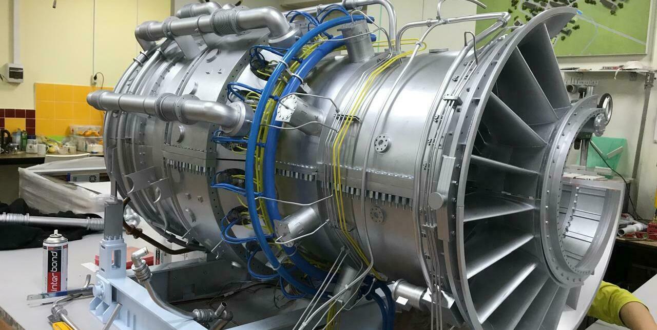 На фотографии изображен макет газовой турбины. Это уменьшенная копия настоящей турбины, выполненная с высокой степенью детализации. Макет установлен на специальном испытательном стенде, где он подключен к различным датчикам и измерительным приборам. Видно, что турбина оборудована различными системами, компрессор и система охлаждения. Макет турбины используются для тестирования и разработки новых технологий, изучения принципов работы двигателя, а также для обучения специалистов и студентов в области авиации. Они позволяют проводить эксперименты в контролируемых условиях, не подвергая риску настоящий двигатель.