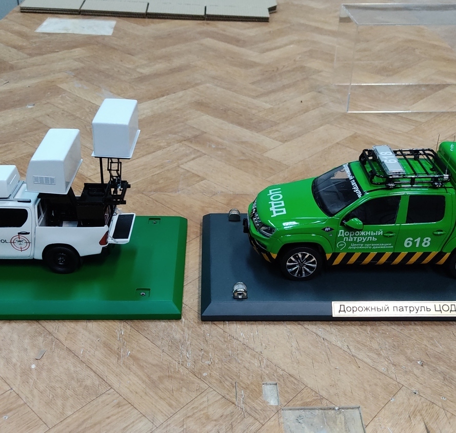 Масштабные модели спецтранспорта: автомобиль «Repellent-Patrol» с оборудованием для мониторинга и патрульный пикап ЦОДД (дорожный патруль, №618) — детализированные макеты для экспозиций и коллекций, изготовленные на заказ в макетной мастерской Maket-modeli.ru Две детализированные масштабные модели спецтранспорта. Слева — белый автомобиль «Repellent-Patrol» с установленным оборудованием: крупными антеннами и техническими блоками на крыше, предназначенными для мониторинга. Справа — зелёный патрульный пикап ЦОДД с маркировкой «Дорожный патруль», номером 618 и фирменными элементами: багажником на крыше, светоотражающими полосами и логотипом ЦОДД. Модели размещены на подставках с информационными табличками, идеально подходят для музейных экспозиций, презентаций и тематических коллекций.