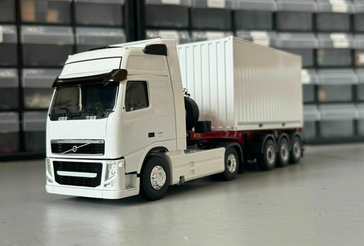 На фото изображён масштабный макет магистрального автопоезда:  • двухосный капотный седельный тягач европейского типа (кабины над двигателем), выполненный по прототипу грузовика Volvo FH; • трёхосный полуприцеп-контейнеровоз с установленным на нём универсальным грузовым контейнером.