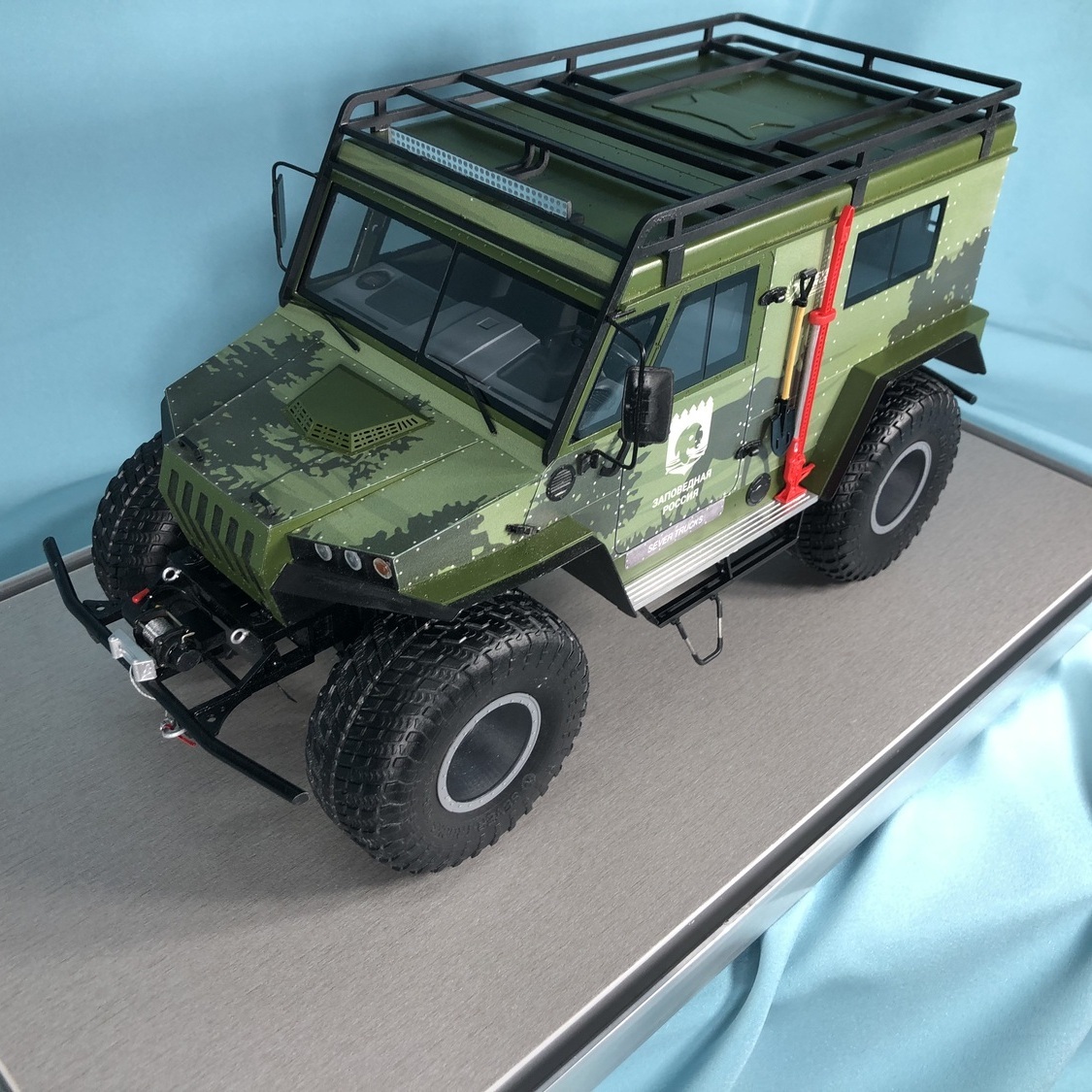 Масштабная модель зеленого экспедиционного внедорожника 4x4 на подставке изготовленный в макетной мастерской maket-modeli.ru Зеленая камуфляжная модель внедорожника 4x4 с экспедиционным багажником и крупными внедорожными шинами, вид сверху на подставке