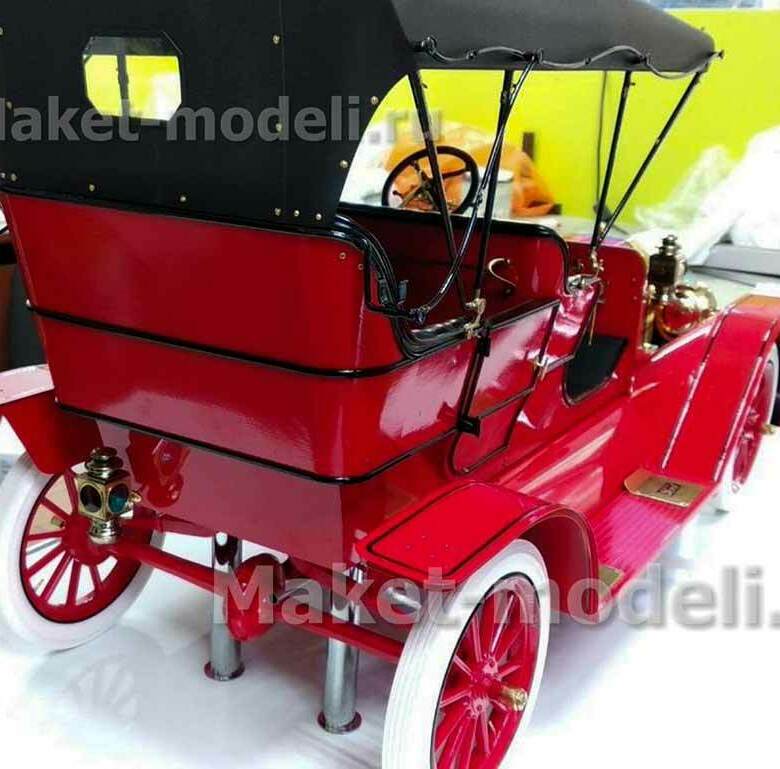 Масштабная модель классического автомобиля Ford Model T 1908 года в ярком красном цвете с чёрным тентом. Отчётливо видны латунные элементы отделки, белые покрышки колёс, аутентичные фары и декоративные накладки. Модель установлена на металлических подставках, подчёркивающих её презентационный характер. Детализирована каждая мелочь — от рулевого колеса до крепёжных элементов. Идеальный экспонат для музея или деловой презентации, демонстрирующий автомобильный дизайн начала XX века. Изготовлена на заказ с сохранением всех исторических особенностей.