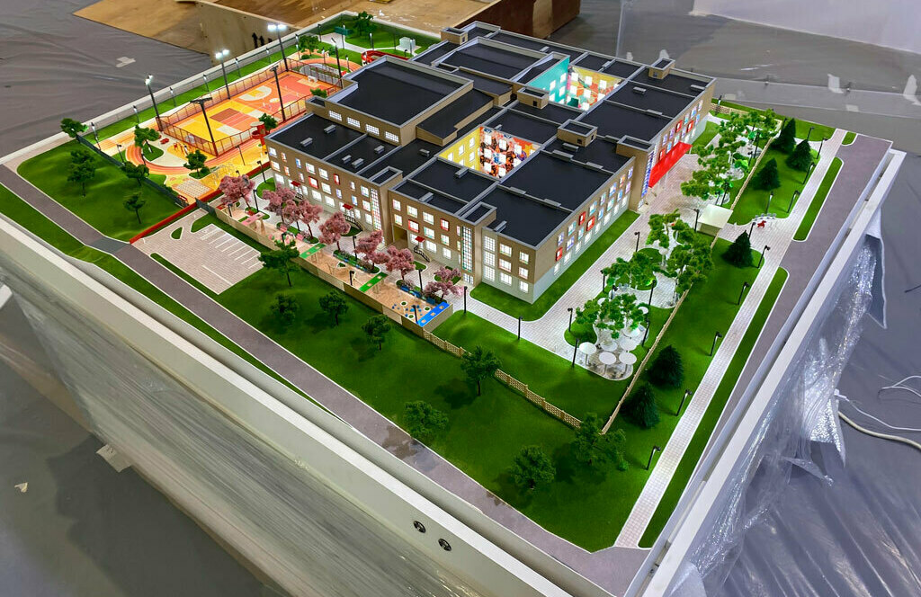 Масштабный архитектурный 3D макет школы и образовательного комплекса с благоустройством двора, ландшафтным дизайном, детской игровой зоной, многофункциональной спортивной площадкой, подъездной дорогой и парковкой — презентация проектного решения для девелопмента и планировочных работ, изготовленный на заказ в макетной мастерской Maket-modeli.ru школы с зелёным газоном, стадионом и сквером. Макет демонстрирует планировку территории вокруг школы и может быть использован для презентации проекта или выставки. Макет школы — детализированный архитектурный 3D макет школьного комплекса с внутренним двором, аллеями и цветущими деревьями, детской площадкой, ограждённой спортивной площадкой с освещением, парковкой и ландшафтным благоустройством для презентации проекта