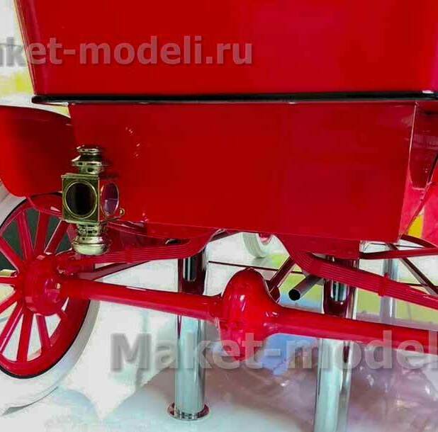 Детально проработанная модель старинного автомобиля в насыщенном красном цвете. Видны характерные элементы: латунная фара, изящные колёсные диски с красными спицами и белыми покрышками, выразительные линии кузова. Модель установлена на металлических подставках, подчёркивающих её презентационный характер. Идеальный экспонат для музея — воплощение автомобильного дизайна эпохи зарождения автопрома, изготовленный на заказ с высокой степенью детализации.