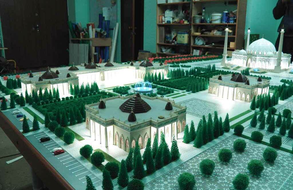 Детальный архитектурный макет комплекса, центральным элементом которого является величественная мечеть с куполом и минаретами. Вокруг мечети расположены симметричные павильоны с купольными крышами, украшенные архитектурными деталями. Территория комплекса тщательно озеленена: миниатюрные деревья и кустарники формируют аккуратные аллеи и зелёные зоны. В центре композиции — декоративный водоём или фонтан, добавляющий изысканности общему виду. Проработаны элементы благоустройства: мощёные дорожки, парковые зоны, парковочные места с макетами автомобилей. Модель демонстрирует гармоничное сочетание религиозной архитектуры и ландшафтного дизайна, подчёркивая масштаб и продуманность планировочного решения. Идеально подходит для презентации архитектурных проектов, привлечения инвесторов и визуализации будущих строительных работ.