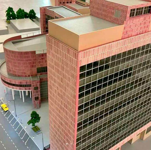 Макет многоэтажного офисного здания с панорамным стеклянным фасадом, округлыми корпусами и проезжей частью с машинами на переднем плане