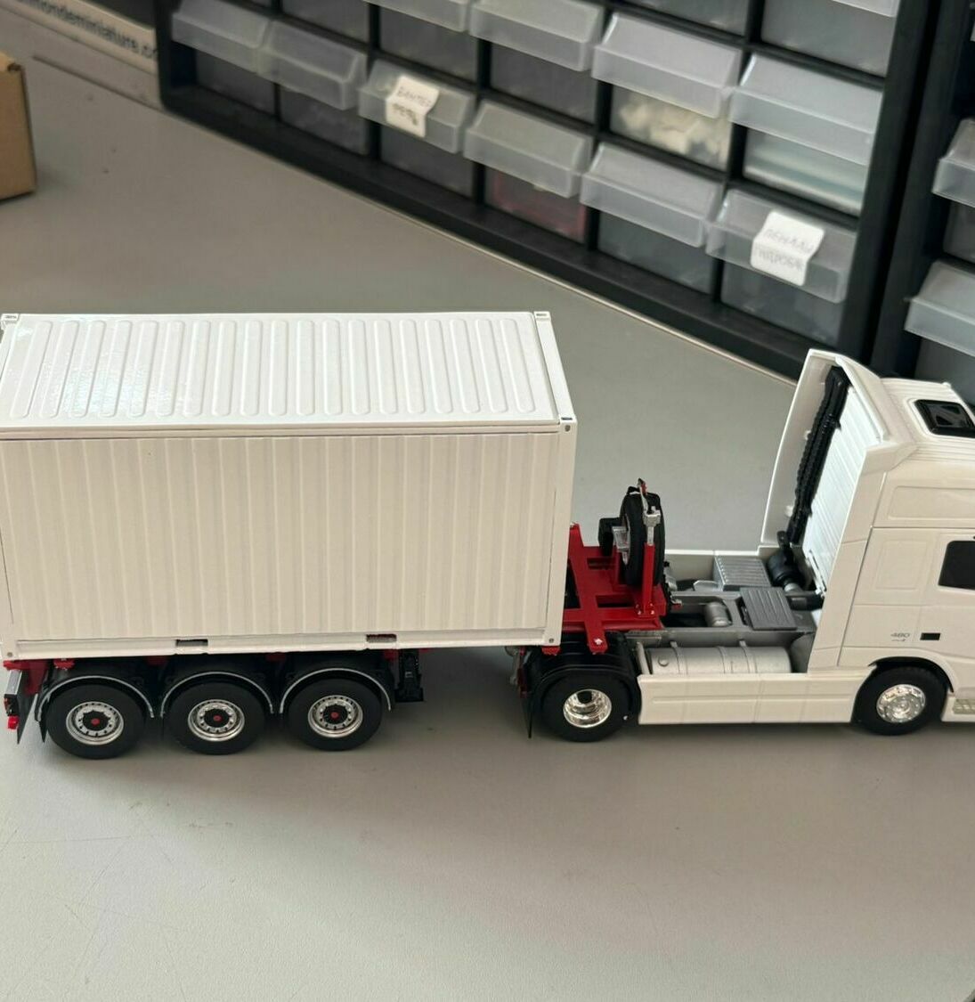 масштабная модель магистрального седельного автопоезда:  • двухосный седельный тягач колесной формулы 4×2 с откинутой (опрокинутой вперёд) кабиной   • трёхосный полуприцеп‑контейнеровоз   • установленный на полуприцепе универсальный крупнотоннажный контейнер (кузов‑контейнер типа «box», близкий к ISO‑контейнеру).