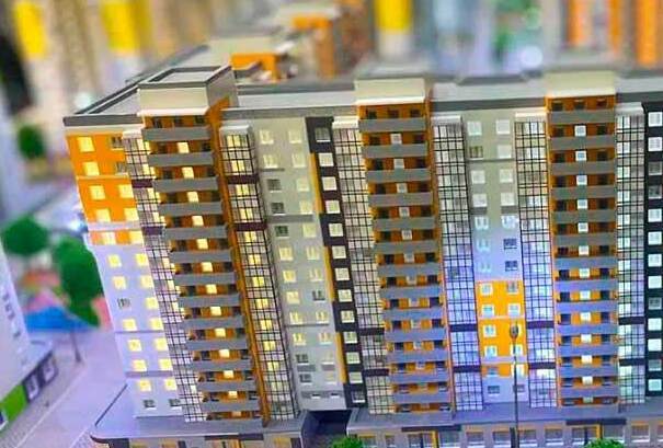 Макет жилого комплекса: масштабная архитектурная модель 10‑этажного многоквартирного дома с застеклёнными балконами, разноцветной отделкой фасадов, торговыми помещениями в цоколе, организованной парковкой и зелёными зонами — модель новостройки для презентации и привлечения инвестиций