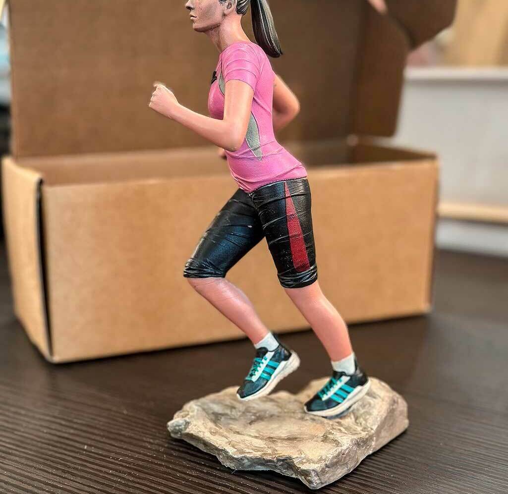 3D-фигурка бегущей девушки, изготовленная на заказ по фото — реалистичная статуэтка на 3D-принтере с детализированной проработкой одежды и позы Статуэтка девушки в спортивной одежде (розовая футболка Saucony, чёрные шорты, кроссовки), запечатлённой в момент бега. Фигурка напечатана на 3D-принтере по фотографии, установлена на основании, имитирующем каменистую поверхность. Пример персонализированной 3D-печати с высокой детализацией: проработаны черты лица, текстура одежды, динамичная поза. Подходит для подарка или коллекционирования.