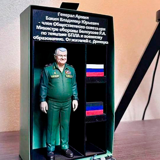3‑D масштабный макет генерала армии В. Ю. Бакина: фигура в военной форме, информационная панель и символика РФ для экспозиций по тематике БПЛА, военного образования и патриотического воспитания 3‑D масштабный макет фигуры генерала армии Владимира Юрьевича Бакина в парадной форме с наградными знаками; на фоне — информационная табличка о статусе члена Общественного совета при Минобороны, справа — полки с флагами РФ; композиция предназначена для музейных, образовательных и патриотических экспозиций