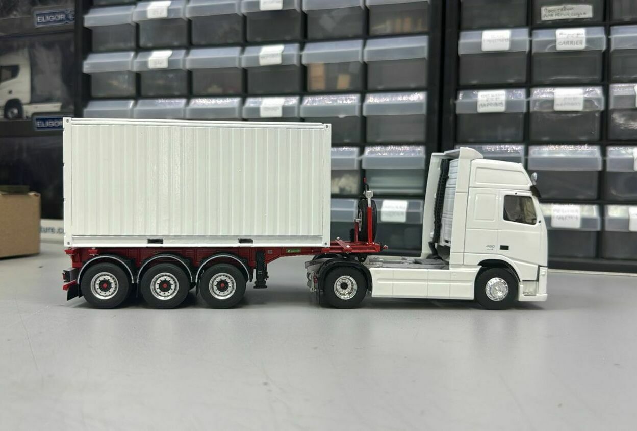 На фото изображена масштабная модель магистрального автопоезда:    • двухосный седельный тягач европейского типа (формула 4×2);   • трёхосный полуприцеп-контейнеровоз;   • установлен универсальный межконтинентальный (морской) ISO‑контейнер.