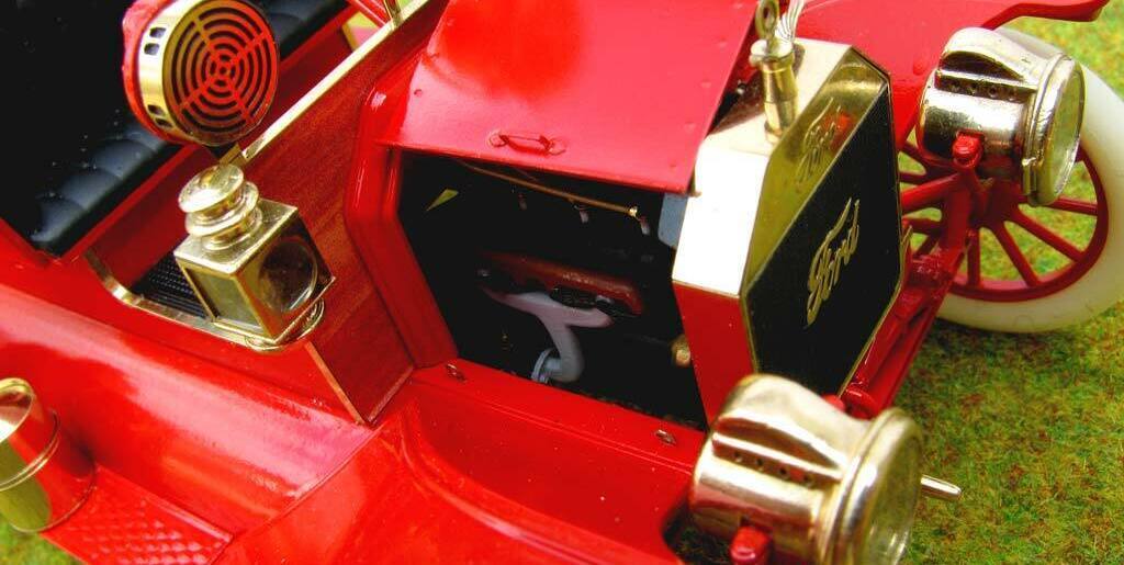3D-масштабная модель коллекционного пожарного автомобиля Ford Model T 1914 года в масштабе 1:24. Видна передняя часть кабины с чёрным стёганым сиденьем, массивным рулевым колесом с красной рукояткой и латунными деталями управления. Присутствуют аутентичные элементы: фара в хромированном корпусе, колокол, рычаги и клапаны пожарного оборудования. Красные акценты сочетаются с полированными латунными вставками, подчёркивая винтажный стиль модели. Идеальный экземпляр для коллекционеров и любителей истории пожарной техники.