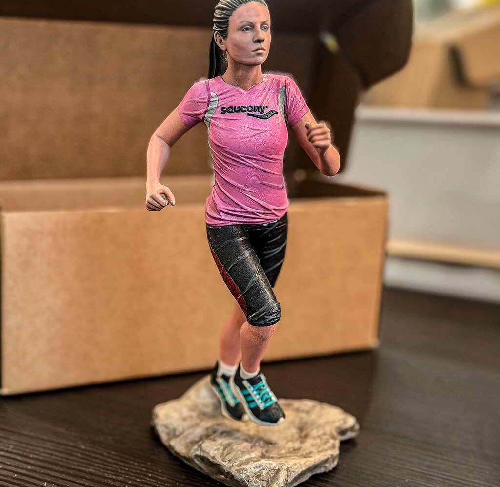 3D-фигурка бегущей девушки, изготовленная на заказ по фото — реалистичная статуэтка на 3D-принтере с детализированной проработкой одежды и позы Статуэтка девушки в спортивной одежде (розовая футболка Saucony, чёрные шорты, кроссовки), запечатлённой в момент бега. Фигурка напечатана на 3D-принтере по фотографии, установлена на основании, имитирующем каменистую поверхность. Пример персонализированной 3D-печати с высокой детализацией: проработаны черты лица, текстура одежды, динамичная поза. Подходит для подарка или коллекционирования.