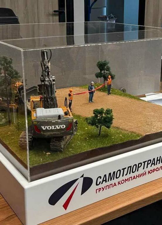 3D-фигурка человека на заказ по фото: реалистичная миниатюра с церемонией перерезания ленты. Кастомная модель в джинсах и стёганой куртке с детализацией одежды и мимики, напечатанная на 3D-принтере для диорамы стройплощадки. Уникальный сувенир для коллекционеров! Реалистичная 3D-фигурка человека, изготовленная по фотографии на 3D-принтере, изображает мужчину в момент перерезания красной ленты — символического акта открытия. Фигурка выполнена с высокой детализацией: мужчина в синей стёганой куртке, светло-зелёной футболке и синих джинсах, с аккуратной сединой и выразительным лицом. В руках держит ножницы, готовясь перерезать ленту. Рядом стоит фигурка строителя в оранжевом жилете и каске, наблюдающего за церемонией. На заднем плане — детализированная модель строительной техники (бульдозер). Композиция идеально подходит для диорамы стройплощадки, коллекционных экспозиций или в качестве оригинального подарка. Пример персонализированной 3D-печати с передачей индивидуальных особенностей и атмосферы события.