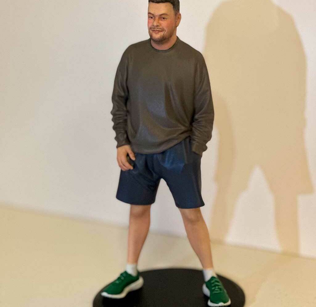 Реалистичная 3D-фигурка человека по фото на заказ — детализированная статуэтка в повседневной одежде, напечатанная на 3D-принтере с высокой точностью. Уникальный сувенир с портретным сходством! 3D-фигурка мужчины, изготовленная по фотографии на 3D-принтере. Фигура в расслабленной позе: одна рука в кармане, другая свободно опущена. Одет в тёмно-серый свитшот, чёрные шорты и зелёные кроссовки. Статуэтка установлена на круглой чёрной подставке. Высокая детализация: проработаны черты лица, текстура одежды, пропорции тела. Пример персонализированной 3D-печати с передачей индивидуального стиля и характера. Подходит для подарка, коллекционирования или декора.