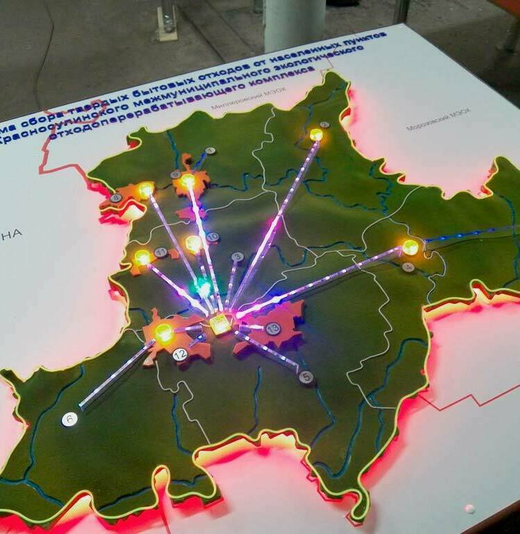 3D масштабный рельефная макет-схема сбора и транспортировки твердых бытовых отходов от населенных пунктов до Красносулинского межмуниципального экологического отходоперерабатывающего комплекса (МЭОК). На макете рельефно выделена территория с подсветкой границ, нанесены маршруты логистики (светящиеся линии), отмечены ключевые населенные пункты и объекты инфраструктуры. Интерактивная инсталляция наглядно демонстрирует структуру межмуниципальной системы обращения с отходами, показывая направление потоков и географическое расположение перерабатывающих мощностей. Используется для презентации экологических проектов и планирования логистики ТБО.