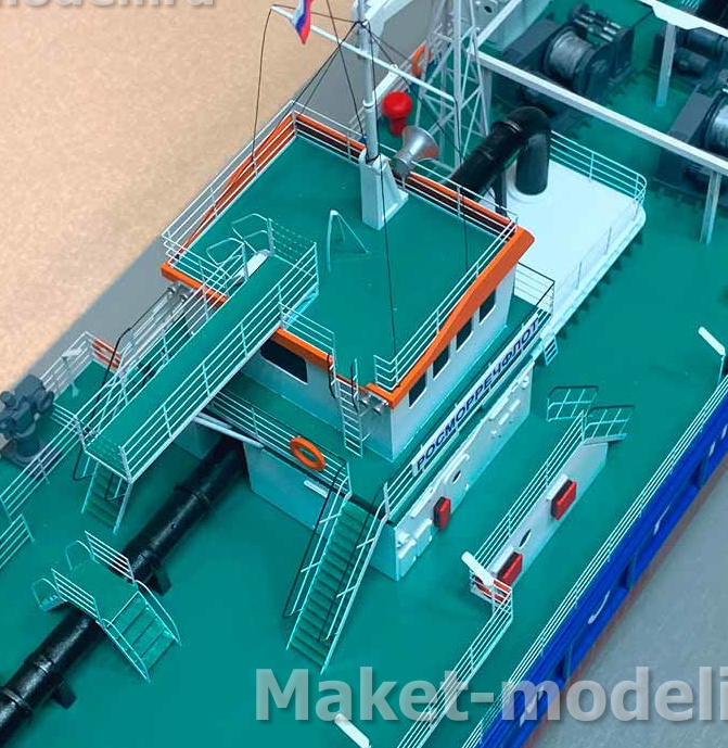 Масштабная модель дноуглубительного судна с детализированной палубой — макет для выставок и моделирования Детальный макет дноуглубительного судна в масштабе, демонстрирующий палубу с инженерными коммуникациями: лебёдки, трубопроводы, спасательные круги, шлюпка, ограждения и лестницы. Видна капитанская рубка с маркировкой, флагшток с российским флагом, элементы палубного оборудования. Модель отражает конструктивные особенности судов для гидротехнических работ — идеально для экспозиций, образовательных проектов и коллекционирования.