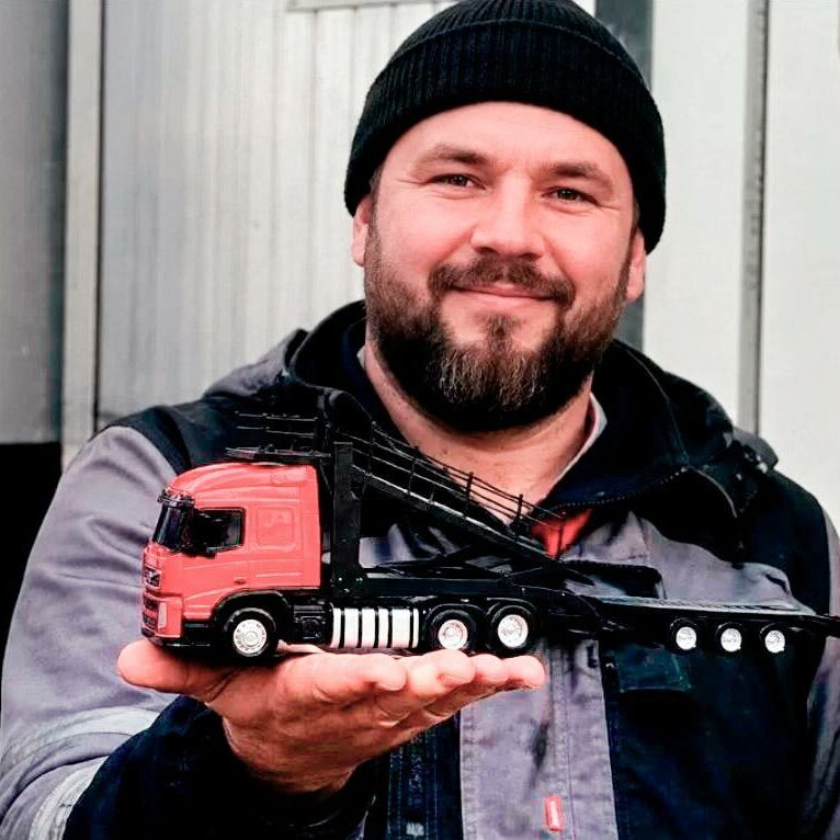 Наш заказчик с коллекционной моделью грузовика из фотополимерной смолы: детализированная фигурка-миниатюра грузового автомобиля в руках, изготовленного на заказ — идеальный подарок для любителей транспорта и коллекционеров Наш заказчик демонстрирует сувенир-миниатюрную модель грузовика тягача-фуры: красно‑чёрная кабина и удлинённый прицеп в ладони — реалистичная фигурка для коллекции или сувенира