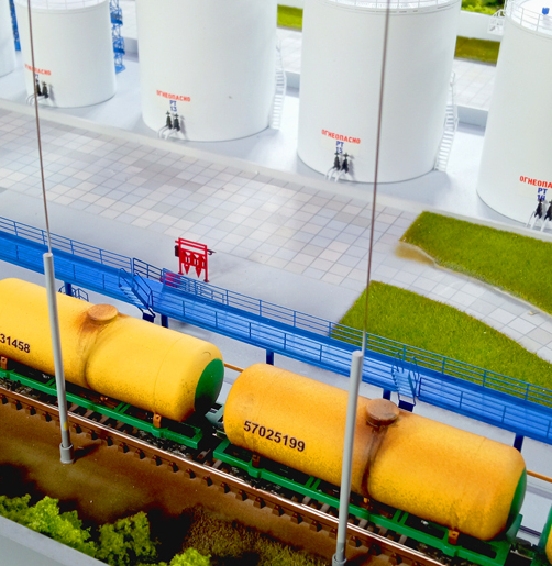 Макет нефтебазы с железнодорожными цистернами – промышленный терминал для хранения топлива, изготовленный на заказ для выставки в г. Москва Детализированный макет нефтебазы: белые вертикальные резервуары для хранения топлива и железнодорожная ветка с желтыми цистернами на территории терминала