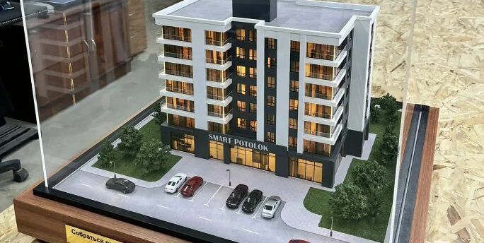 3D-масштабный макет современного многоэтажного жилого здания с подсветкой фасадов. Модель демонстрирует планировку комплекса: главный корпус с балконами и большими окнами, входная группа, крытая парковка с несколькими автомобилями, благоустроенные зелёные зоны с деревьями и кустарниками по периметру. Видны элементы городской инфраструктуры — проезжая часть с разметкой, тротуар, уличные фонари. Макет выполнен с высокой детализацией, включая текстуры фасадов, ландшафт и миниатюрные автомобили, что позволяет наглядно представить будущий объект и его интеграцию в городскую среду. Идеален для презентации девелоперских проектов инвесторам и будущим жильцам.