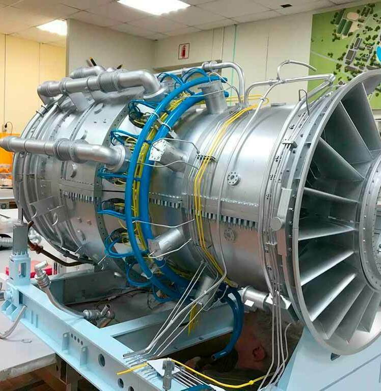 Детализированный макет газовой турбины промышленного оборудования: отчётливо видны лопатки турбинного колеса, корпус с рёбрами жёсткости, разветвлённая система трубопроводов (синие и жёлтые линии), крепёжные элементы, монтажные узлы и элементы системы охлаждения. Модель установлена на демонстрационной раме, демонстрирует внутреннюю компоновку и ключевые узлы газотурбинной установки. Подходит для использования на отраслевых выставках, в образовательных целях, для презентаций инженерных решений в сфере энергетического оборудования. Проработка мелких деталей подчёркивает сложность и точность конструкции промышленного агрегата.