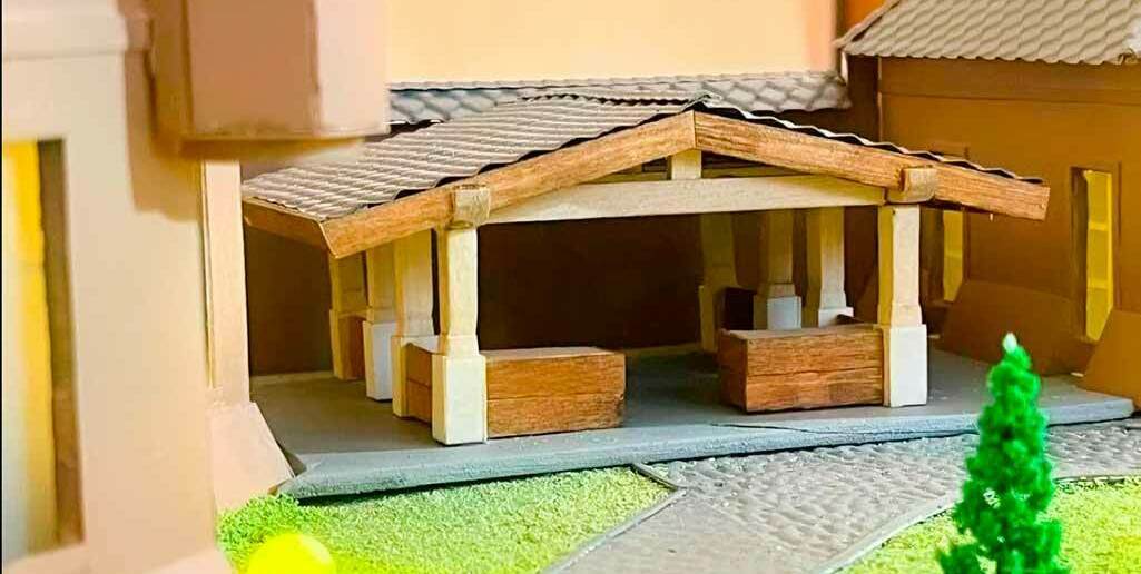 етальный архитектурный макет загородного дома с навесом и ландшафтным дизайном — образец для презентации проектов частной застройки Масштабная модель участка с загородным домом, включающая детализированный навес с деревянными колоннами и балками, имитирующими натуральную древесину. Рядом с навесом — аккуратно выложенные дорожки из миниатюрной брусчатки, ведущие к дому. В композиции присутствуют элементы ландшафтного дизайна: искусственная зелёная трава, стилизованное хвойное дерево, чёткие границы газона. Крыша навеса выполнена из текстурированного материала, имитирующего черепицу. Модель демонстрирует продуманную организацию придомовой территории, сочетая архитектурные элементы с озеленением — идеально для визуализации проектов частных домов и планирования малых архитектурных форм.