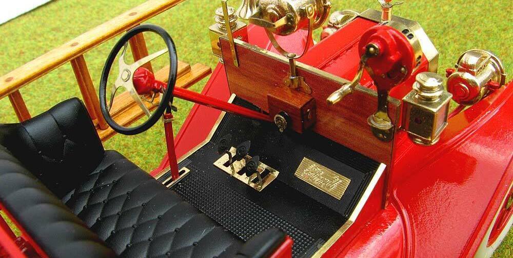 3D-масштабная модель коллекционного пожарного автомобиля Ford Model T 1914 года в масштабе 1:24. Видна передняя часть кабины с чёрным стёганым сиденьем, массивным рулевым колесом с красной рукояткой и латунными деталями управления. Присутствуют аутентичные элементы: фара в хромированном корпусе, колокол, рычаги и клапаны пожарного оборудования. Красные акценты сочетаются с полированными латунными вставками, подчёркивая винтажный стиль модели. Идеальный экземпляр для коллекционеров и любителей истории пожарной техники.