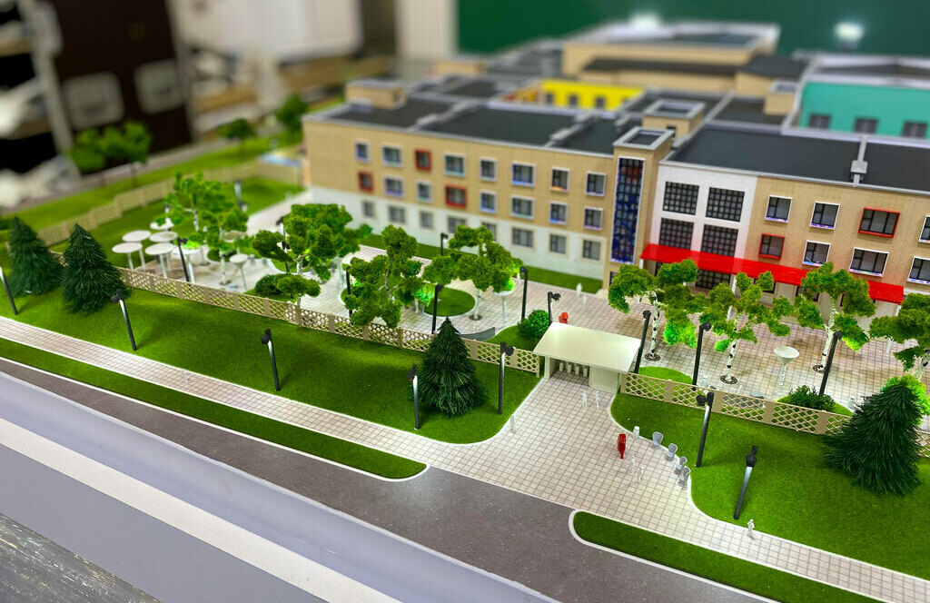 Архитектурный масштабный 3-D макет общеобразовательной школы — ландшафтный дизайн, внутренний двор, детская игровая зона, многофункциональная спортивная площадка и парковка Детализированный архитектурный макет школьного комплекса: трехэтажное здание с маркизами, благоустроенный внутренний двор с мощеными аллеями, деревьями, уличными светильниками, беседками, детской игровой зоной, подъездной дорожкой и парковкой для презентации проектного решения.